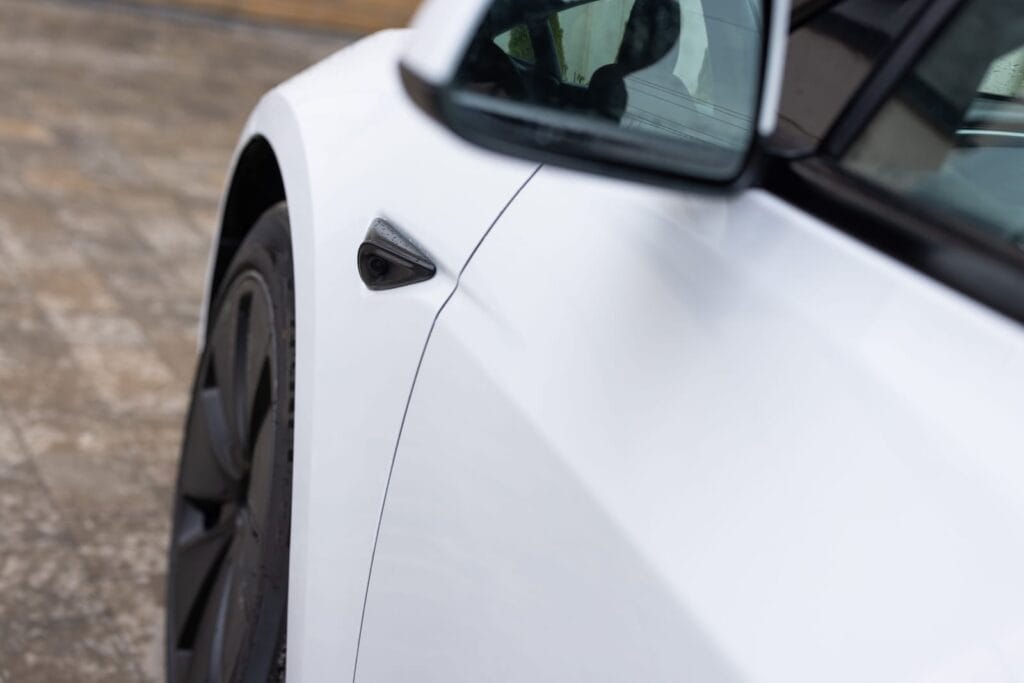 White Tesla Model 3 closeup photo of driver side mirror and front left tire.